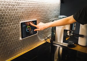 Modern kitchen scene featuring a hand using a tablet to control a smart home system.