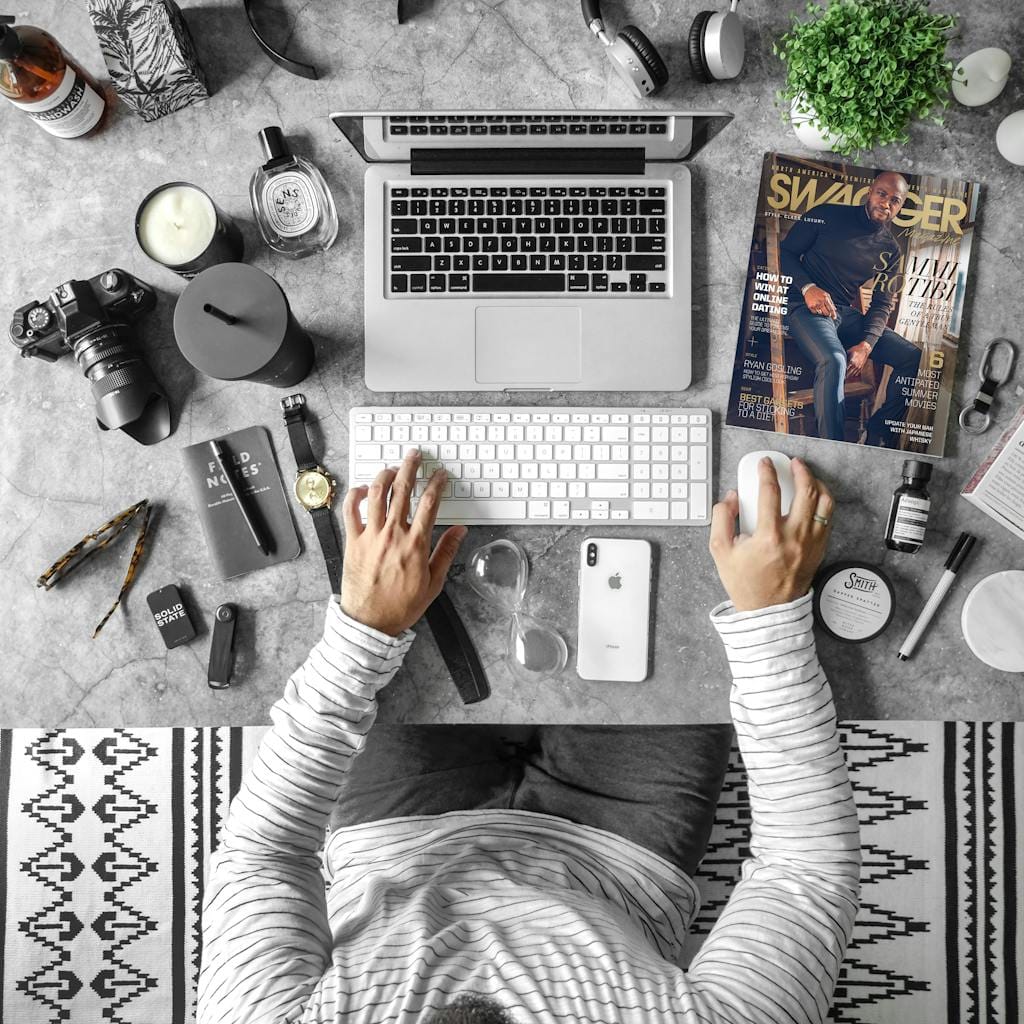 Overhead view of an organized desk with tech gadgets, fashion magazine, and accessories for modern working lifestyle.